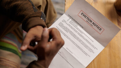 Person sitting on comfortable chair and reading eviction notice placed on wooden table. Hands and partial view of person visible, creating a sense of urgency.