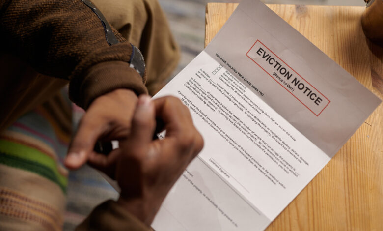 Person sitting on comfortable chair and reading eviction notice placed on wooden table. Hands and partial view of person visible, creating a sense of urgency.