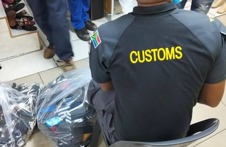 Customs official sits alongside bags of footwear during a joint operation targeting counterfeit goods in Johannesburg CBD on 13 October 2026. Photograph: SAPS.